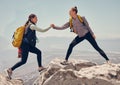 Happy women help while hiking up a rocky mountain in nature with backpack. Females friends exercise in nature park