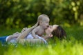 Woman holding in arm a baby in a garden and lying on the grass