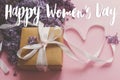 Happy women`s day floral greeting card. Handwritten greetings on lilac flowers and gift box on pink paper. International women`s