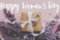 Happy women`s day floral greeting card. Handwritten greetings on lilac flowers and gift box on pink paper. International women`s