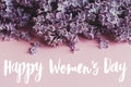 Happy women`s day floral greeting card. Handwritten greetings on lilac flowers purple border on pink paper. International women`