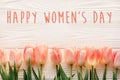 Happy women`s day text on pink tulips on white rustic wooden bac