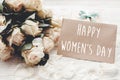 Happy Women`s Day text sign on craft greeting card and white roses bouquet, gift box on wooden background. International womens