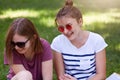Happy women talking and laughing in park, sitting on grass, wear casual clothes and sunglasses, hear funny joke, remember schol Royalty Free Stock Photo