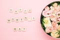 Happy womens day lettering on the wooden squares with letters on the pink background and big round box with red flowers
