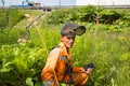 Happy worker in bright orange overalls sitting with a motorcycle mower on the background of mowing tall grass of borscht weed