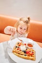 Happy 3 year old girl eat. Breakfast in cafe. Classic Viennese waffles with ice cream, berries and Maple syrup. Table in Royalty Free Stock Photo