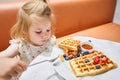 Happy 3 year old girl eat. Breakfast in cafe. Classic Viennese waffles with ice cream, berries and Maple syrup. Table in Royalty Free Stock Photo