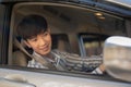 A happy young adult Asian man in casual outfit is driving a car, looking at the side-view mirror Royalty Free Stock Photo
