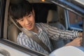 A happy young adult Asian man in casual outfit is driving a car, looking at the side-view mirror Royalty Free Stock Photo