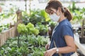 Happy young adult Asian woman with medical face mask buying pot, little tree pot, pot of flowers or plants at greenhouse or garden Royalty Free Stock Photo