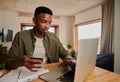 Happy young adult black male making online payment on laptop in modern apartment. Royalty Free Stock Photo