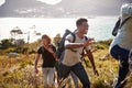 Happy young adult friends hiking uphill near the coast, close up, backlit Royalty Free Stock Photo