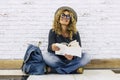 Happy young adult traveler woman sitting on the floor reading a book. Travel female people lifstyle. Curly hair and trendy hat Royalty Free Stock Photo