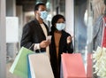 Happy young african american couple of shoppers in protective mask walk in mall, hold colorful bags Royalty Free Stock Photo