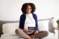 Happy young african american curly pregnant woman with belly in casual sit on bed with ultrasound picture Royalty Free Stock Photo