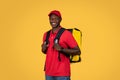 Happy young african american deliveryman in red uniform with big backpack, enjoy work