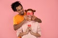 Happy young African American man is covering red haired caucasian woman eyes with surprise and giving her heart cards on Royalty Free Stock Photo