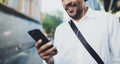 Happy young African American man in headphone walking at sunny city and enjoying to listen to music on his mobile phone Royalty Free Stock Photo