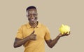 Happy young African American man holding piggy bank, smiling and giving thumbs up Royalty Free Stock Photo