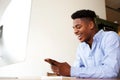 Happy young african american man sitting with mobile phone at computer Royalty Free Stock Photo