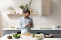 Happy young African American man using cellphone, cooking in kitchen. Royalty Free Stock Photo