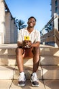 Happy, young African American man using mobile phone outdoors sitting on stairs. Vertical image. Royalty Free Stock Photo