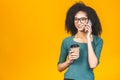 Happy young african american woman casually dressed standing isolated over yellow background, talking on mobile phone, holding Royalty Free Stock Photo