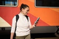 Happy young African American woman passenger using smart mobile phone in the platform of a railway train station. Royalty Free Stock Photo
