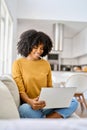 Happy young African American woman sitting on couch at home using laptop. Royalty Free Stock Photo