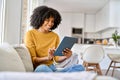 Happy young African American woman sitting on sofa at home using digital tablet. Royalty Free Stock Photo