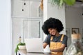Happy young African American woman talking on phone using laptop in cafe. Royalty Free Stock Photo