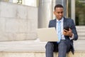 Happy young African businessman working with laptop and phone on the stairs outdoors Royalty Free Stock Photo