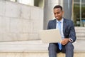 Happy young African businessman working with laptop while sitting on the stairs outdoors Royalty Free Stock Photo