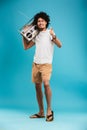 Happy young african curly man holding boombox pointing.