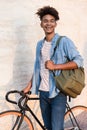 Happy young african guy walking with bicycle outdoors on the street