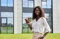 Happy young African lady using mobile phone standing outdoors. Royalty Free Stock Photo