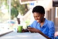 Happy young african woman sitting at outdoor cafe using mobile phone Royalty Free Stock Photo