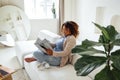 Happy young african woman sitting on sofa indoors at home while reading magazine or book Royalty Free Stock Photo