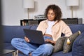 Happy young African woman using laptop computer sitting on sofa at home. Royalty Free Stock Photo