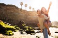 Happy young arab guy holding on back asian woman, have fun together on beach, enjoy freedom