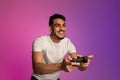 Happy young Arab guy with joystick playing video game in neon light. Modern hobbies concept