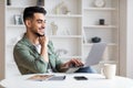 Happy young arab man with beard looks at laptop, have chat in social networks in home office interior Royalty Free Stock Photo