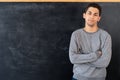 Happy young arab man standing with crossed arms on blackboard background, education concept, serious male teacher or Royalty Free Stock Photo