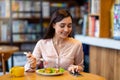 Happy young arab woman texting on smartphone while eating salad in cafe, using an application to send an sms Royalty Free Stock Photo