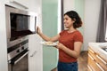 Happy Young Arab Woman Warming Food In Microwave In Kitchen Royalty Free Stock Photo