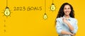 Happy young arabic lady point finger at 2023 goals inscription with light bulbs, checklist with free space