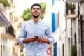 Happy young arabic man laughing with mobile phone and earphones in the city