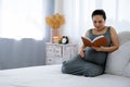 Happy young Asia pregnant woman holding and reading red book and sitting on white bed Royalty Free Stock Photo