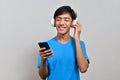 Happy young Asian boy teenager holding a mobile phone, listening to music with his headphones Royalty Free Stock Photo